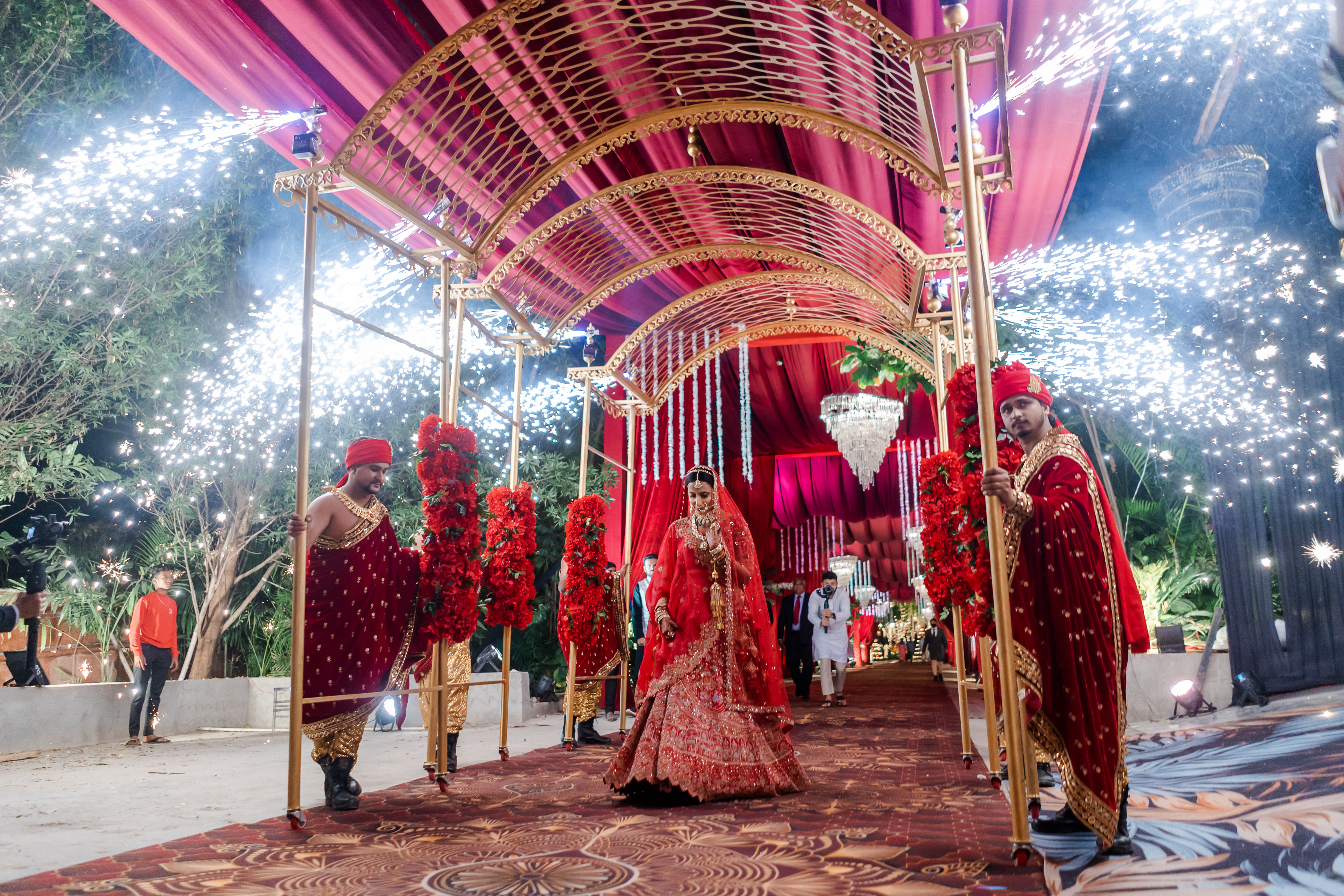 A bride entering under a golden mandap amid sparklers
