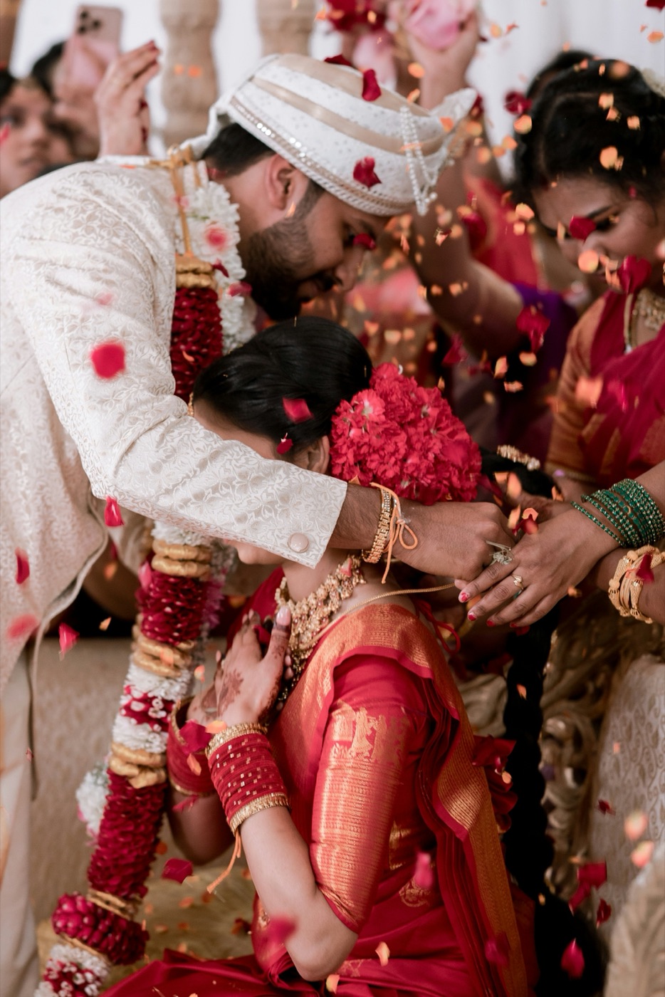 A groom helping the bride up during the wedding ceremony as guests shower them with rose petals