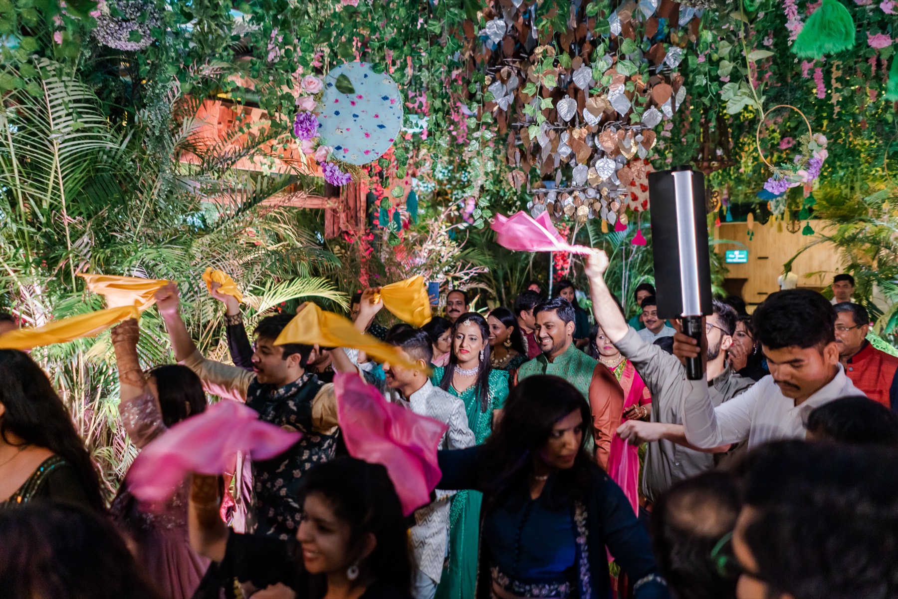 Crowd dancing with pink and yellow napkins under floral decor